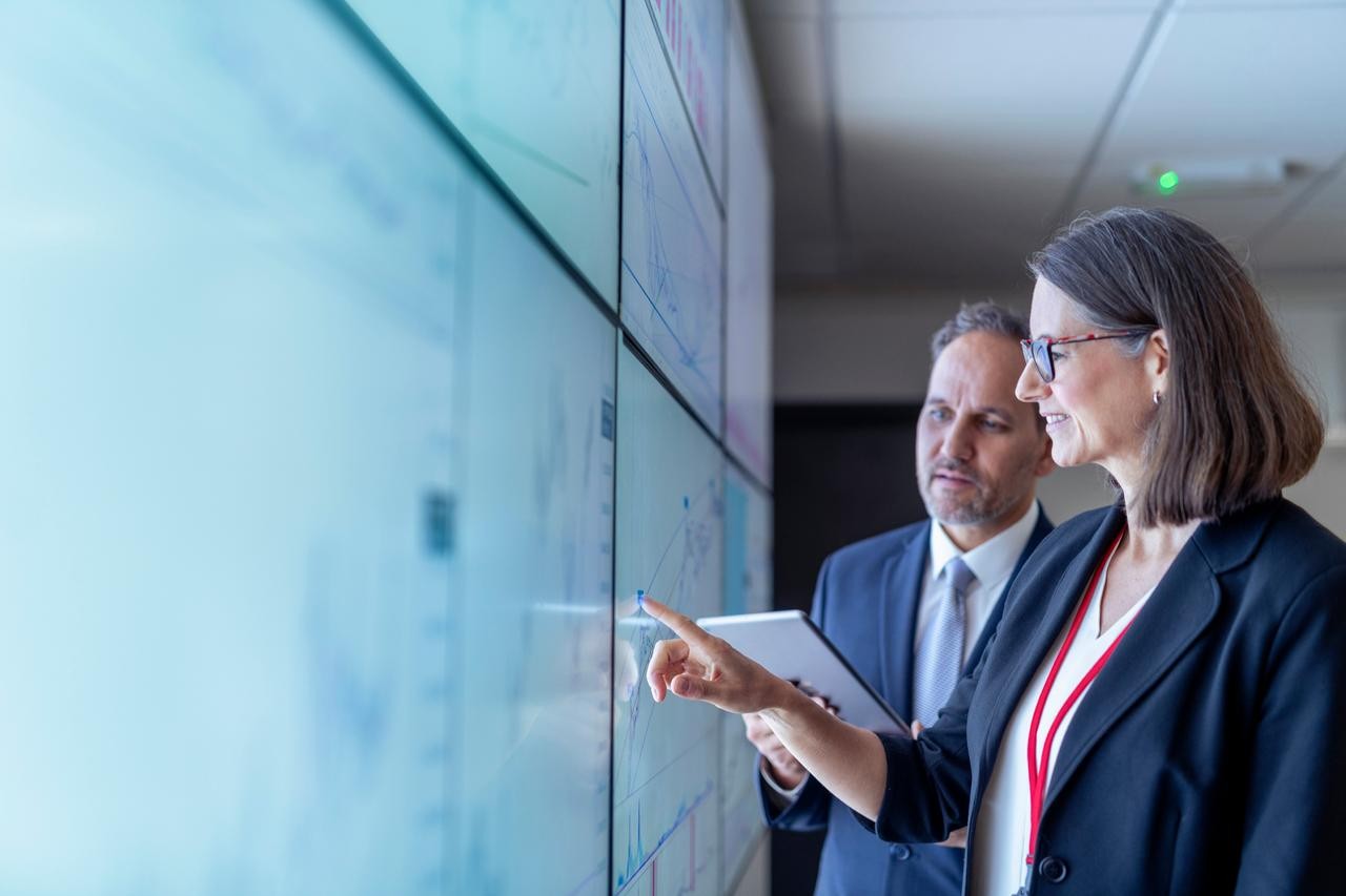 one woman and one man looking at a screen. The woman is pointing something on the screen 