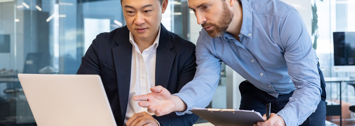 2 businessmen talking in front of a laptop in an office 