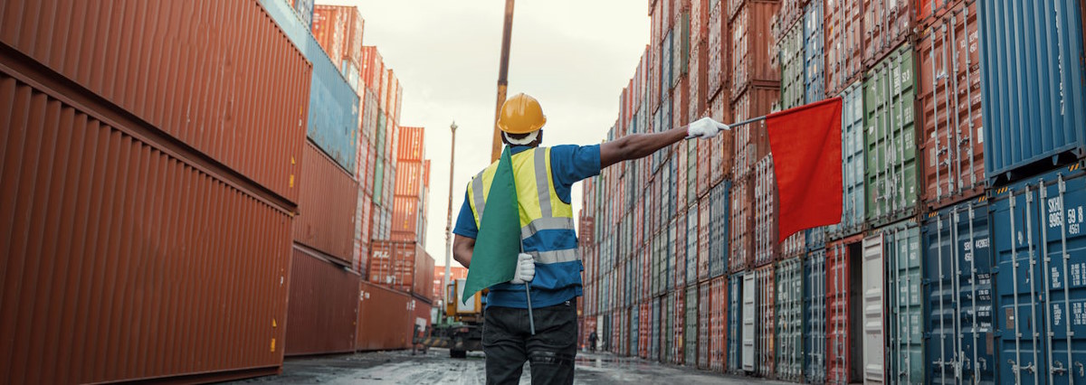 Docker working in industrial harbor waving red flag in front of containers