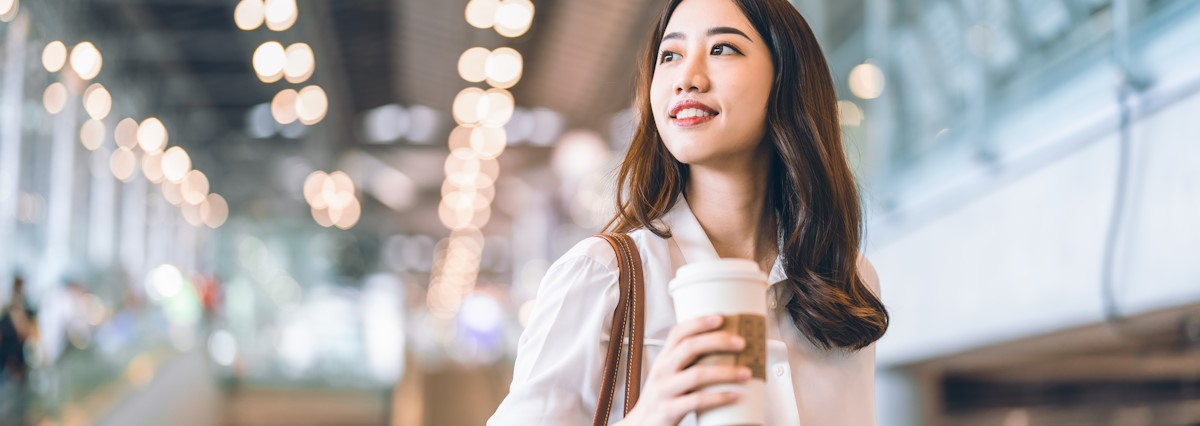 smiling asian woman walking with a coffee in hands