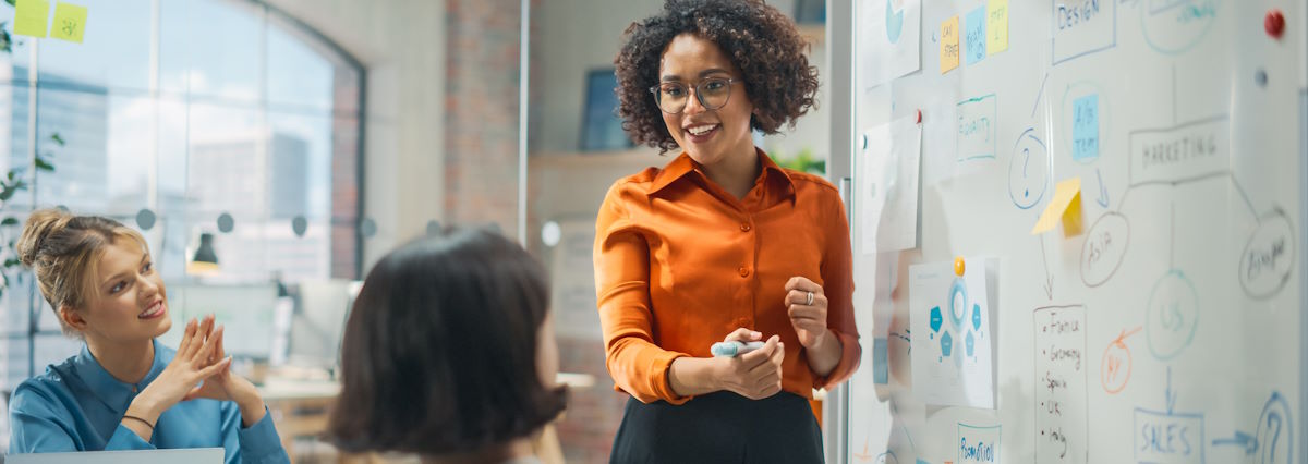 smiling professional woman in frond of whiteboard exchanging with colleagues